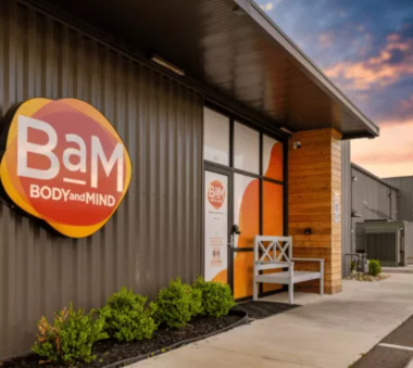 Modern building exterior with a sign reading 'BAM Body and Mind' and a bench by the entrance at sunset
