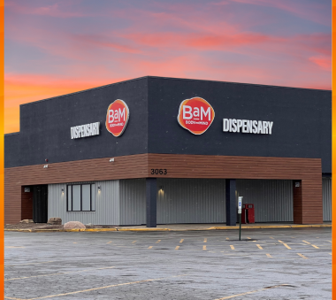 A corner building with 'BAM Body and Mind' logos on a dark upper facade and a sunset sky in the background