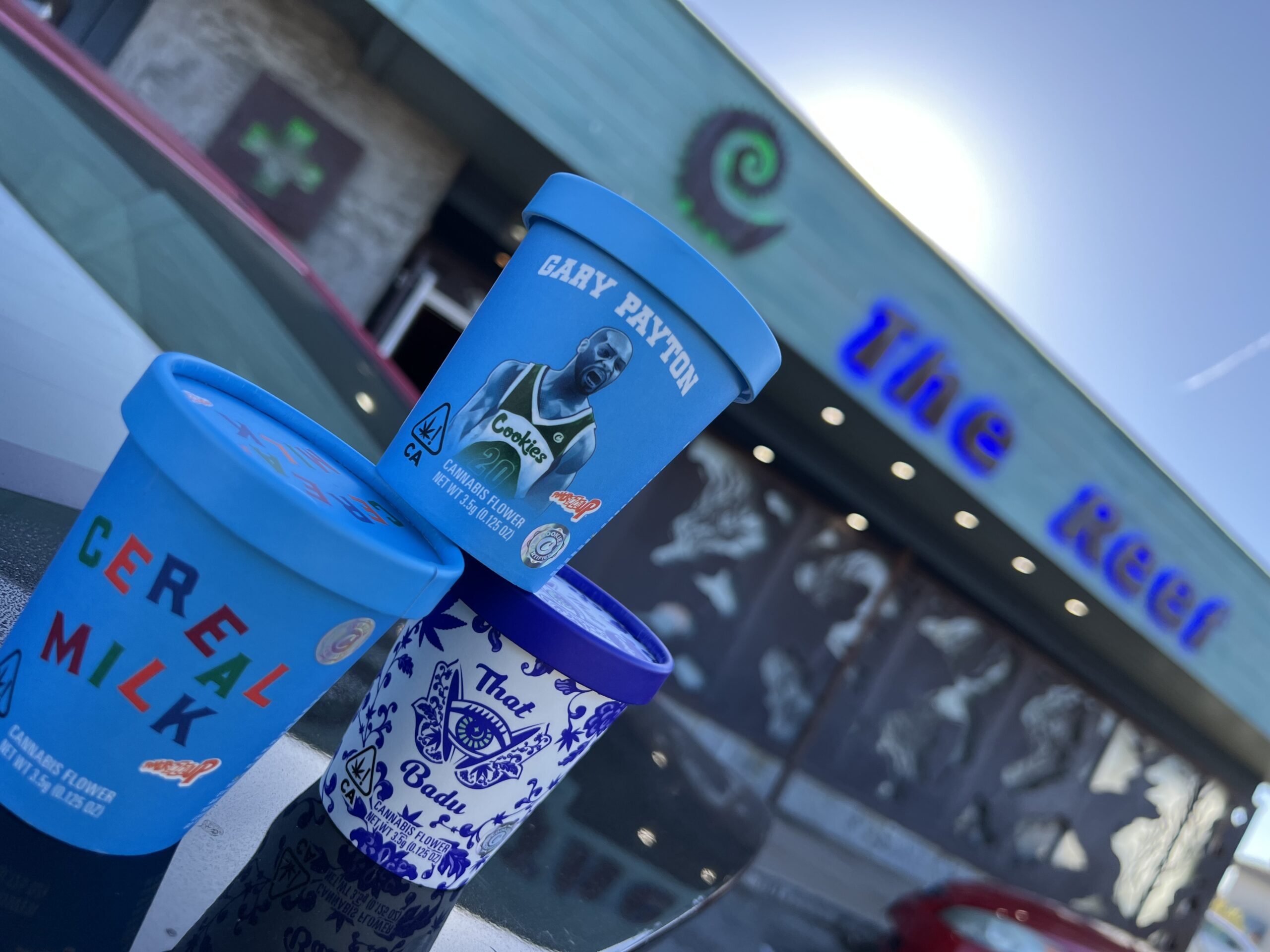 Three colorful containers stacked on a reflective surface with a building and a bright sky in the background