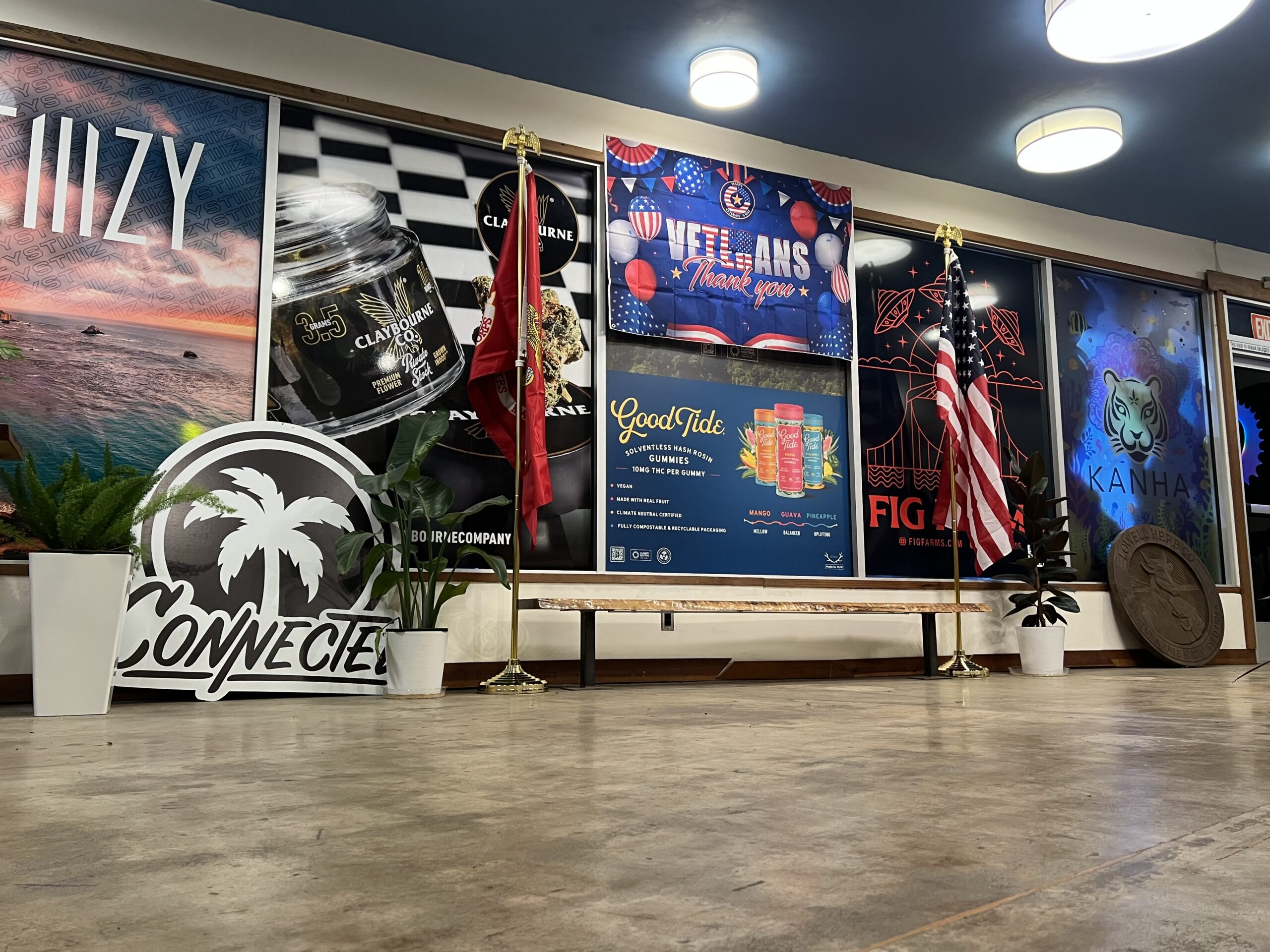 Two flags stand beside a bench in front of a wall with colorful posters and plants on a polished floor