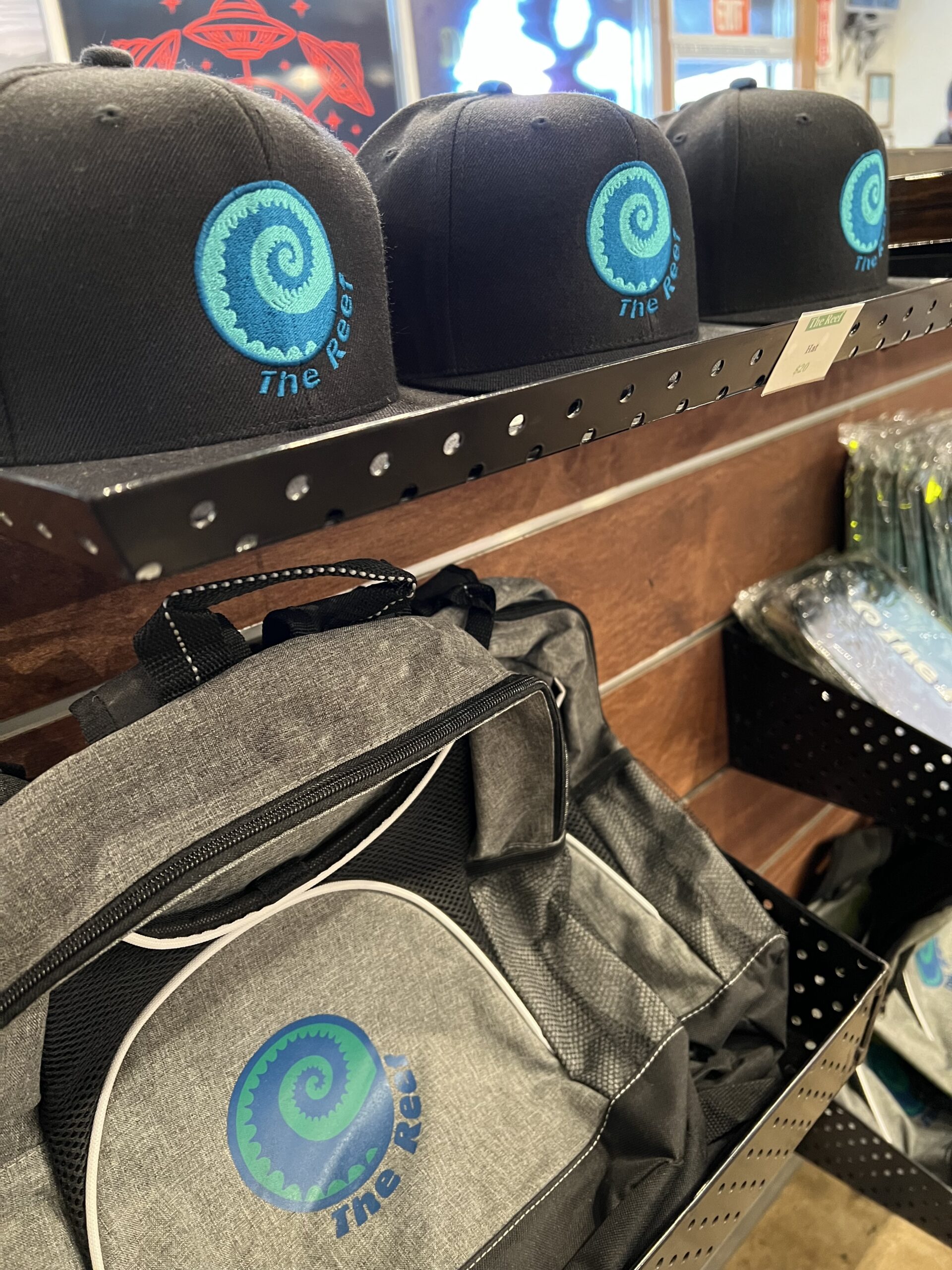 Shelf display featuring hats and backpacks with a blue spiral logo and the text 'The Reef'